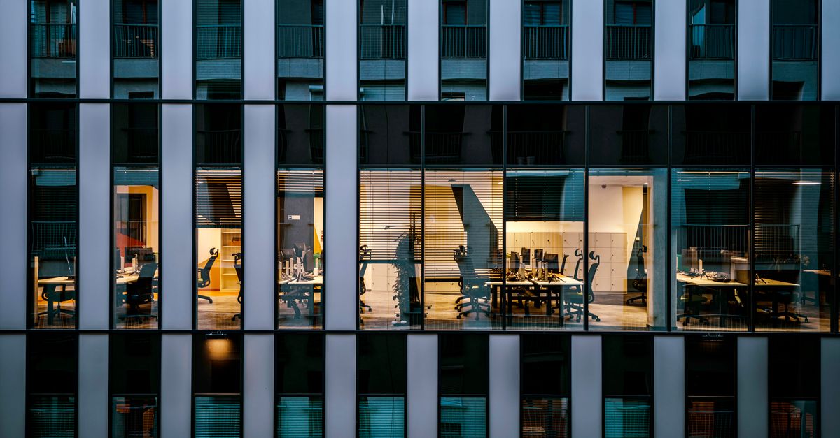 Illuminated office inside a modern glass building exterior, showcasing architecture and workspace design.